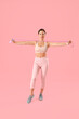 Sporty young woman training with skipping rope on pink background