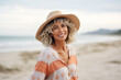 medium shot portrait photography of a pleased woman in her 50s that is wearing casual beach attire, straw hat against strolling along a tranquil beach background