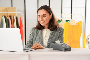 Wall Mural - Female seller working with laptop at counter in clothing shop