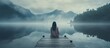 Back view of fashioned young woman sitting on wooden dock looking at view on a misty morning Female hipster with brown hat relaxes on the edge of jetty admiring foggy lake Wonderful nature geta