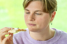 In This Close-up Image, A Woman In A Lavender Sweater Appears To Be Savoring A Bite Of Food, Her Eyes Closed In Appreciation Of The Taste. The Soft, Natural Light Suggests A Comfortable, Daylit
