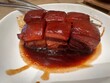 blurred traditional Chinese red braised pork belly called Hong Shao Rou, cut into small pieces Served on a white plate.