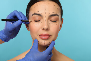 Canvas Print - Doctor with pencil preparing patient for cosmetic surgery operation on light blue background, closeup