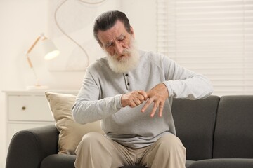 Poster - Senior man suffering from pain in hand on sofa at home. Rheumatism symptom