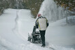 © AlexGo - Man removes snow with a snowblower rear view. working with a gasoline snow blower after the severe winter storm in the city. Clearing the area from snowfall.