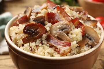 Tasty quinoa porridge with fried bacon and mushrooms in bowl, closeup