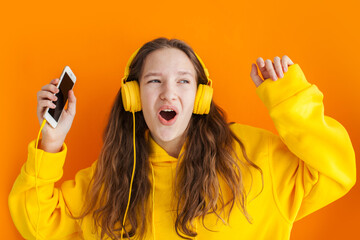 Wall Mural - curly teenager girl has fun indoor, listens pleasant melody in headphones