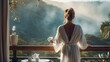 Back view of a happy woman with a cup of coffee or tea in a white towel after showering, standing on an open resort balcony