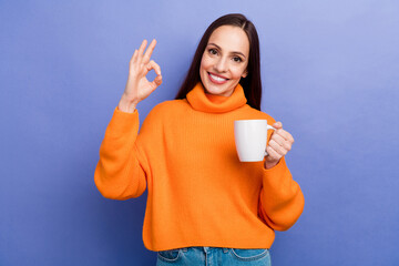 Sticker - Photo happy woman in orange knit sweater show okey sign hold white cup of morning coffee like tradition isolated on violet color background