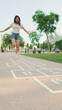 © Andrii Nekrasov - Joyful beautiful brunette girl dressed in casual clothes playing hopscotch game outdoors, having fun