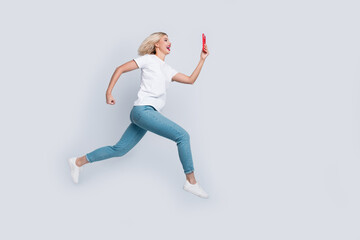 Wall Mural - Full size photo of cheerful woman dressed white t-shirt denim pants fast run look at smartphone isolated on white color background