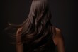 Portrait of brunette woman from back with long groomed and waving hair on dark background.