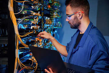 Cables management. Young man is working with internet equipment and wires in server room