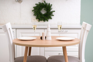 two glasses of champagne, two white plates on round wooden table. christmas home interior. ceramic v