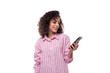 © Ivan Traimak - young confident brunette curly businesswoman dressed in a striped pink shirt writes a message on the phone