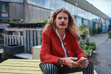 Longhaired man wearing trendy clothes reading message while looking at the camera