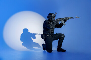 Wall Mural - Action photo, Soldier in black uniforms with weapon standing on his knee in studio. Concept Military warrior army tactical force to fight crime in city