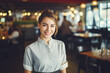 A portrait of a smiling young woman waitress in uniform inside a modern, stylish and bright restaurant. 