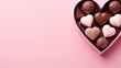 Heart-shaped chocolate box, with chocolate candies inside, isolated on plain pink background.