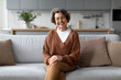 © Home-stock - Smiling senior woman wearing eyeglasses looking at camera, happy elderly lady sitting on sofa at home, resting in living room interior
