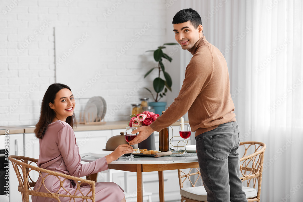 Young man giving his girlfriend glass of wine in kitchen