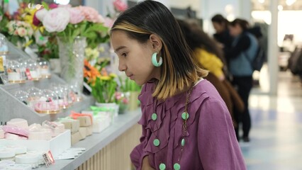 A little fashionista chooses and looks at cans of natural cosmetics in a large shopping center. Fair with cosmetics for child care from various manufacturers.