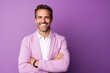 © Loli - Portrait of a smiling young man standing with arms folded against purple background