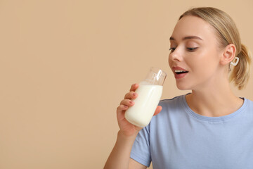 Wall Mural - Pretty young woman drinking milk on beige background