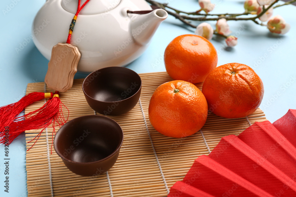 Teapot with cups, mandarins and sakura on blue background. New Year celebration