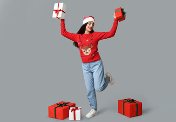 Sticker - Happy young woman in Christmas sweater with gift boxes on grey background