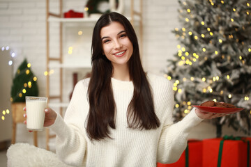 Poster - Beautiful young woman with glass of milk and cookies at home on Christmas eve