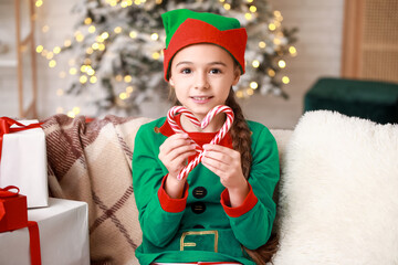 Sticker - Cute little girl in elf costume with candy canes at home on Christmas eve