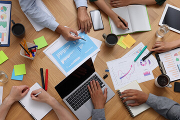 Canvas Print - Team of employees working together at wooden table, top view. Startup project