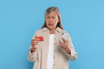 Canvas Print - Worried woman with credit card and smartphone on light blue background. Be careful - fraud