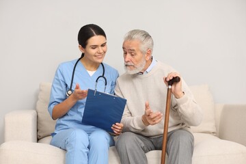 Poster - Smiling nurse with clipboard assisting elderly patient on sofa indoors