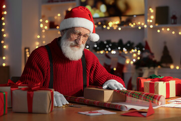 Poster - Santa Claus wrapping gift at his workplace in room decorated for Christmas