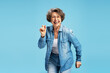 © Maria Vitkovska - Smiling confident senior woman, happy active grandmother wearing stylish denim jacket, eyeglasses dancing isolated on blue background. Positive lifestyle concept