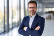 © Hung - Portrait of confident mature businessman with arms crossed standing in office.