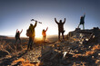 Big group of young hikers with backpacks are standing with open arms in winner poses at sunset mountain