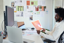 Designer Evaluating Graphic Print. Black businessman reviewing print sample at desk