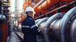 Male worker stands inspection at long steel pipe and pipe elbow in gas station factory between refinery valves of oil pipeline recording inspection and gas industry.