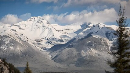 Wall Mural - Cinemagraph of white clouds in blue sky moving over snowcapped mountain range and treetops