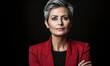 Confident mature businesswoman with stylish short gray hair wearing a red blazer over a black shirt, poised against a dark brown backdrop