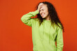 Young sad woman of African American ethnicity she wear green hoody casual clothes put hand on face facepalm epic fail mistaken omg gesture isolated on plain red orange background. Lifestyle concept.