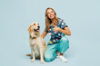 Full body young veterinarian woman wearing uniform stethoscope heal exam hug cuddle embrace kneeling near retriever dog show thumb up isolated on plain blue background studio. Pet health care concept.