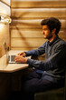 © carlesmiro - Side view of focused young male typing on laptop while working on project in cozy workplace with wooden interior.