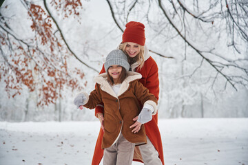 Front view, standing. Mother and her daughter is on the winter meadow and forest