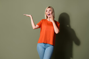 Poster - Photo portrait of attractive young woman shocked palm hold empty space dressed stylish orange clothes isolated on khaki color background