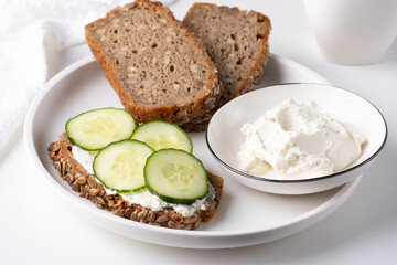 Rye bread with cream cheese and cucumbers on a white table. Whole grain rye bread with seeds