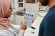 Muslim woman general practitioner in headscarf showing medical questionnaire on tablet screen to adult male patient and asking questions about pain intensity, focus tablet computer